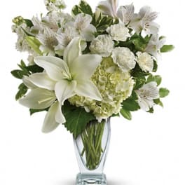 White lilies and mixed white flowers in a clear glass vase