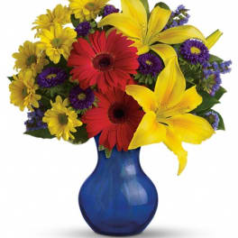 Bouquet of yellow lilies, red gerberas, and purple daisies in a blue vase