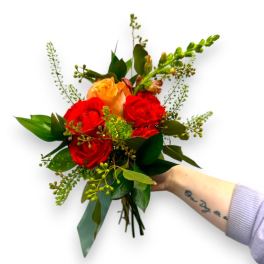 Handheld bouquet of red and peach roses with greenery