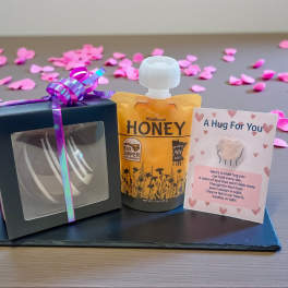 Gift set with honey, a small boxed item, and a card on a tray with pink petals
