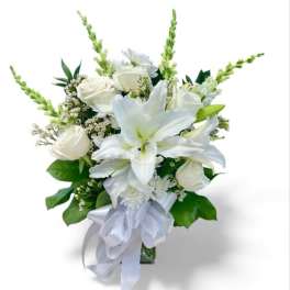 White lilies and roses arranged in a glass vase with a white ribbon