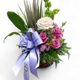 Basket arrangement of pink and white roses with a lavender ribbon