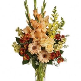 Bouquet of peach roses, gerbera daisies, and orange flowers in a clear glass vase