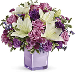Purple and white bouquet of lilies and roses in a lavender vase
