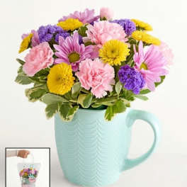Mixed pink, purple, and yellow flowers in a mint mug vase