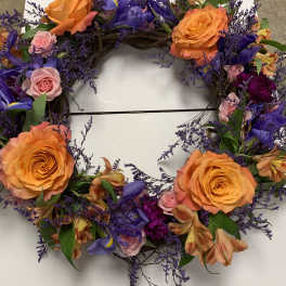 Circular floral wreath with orange roses, purple flowers, and pink accents