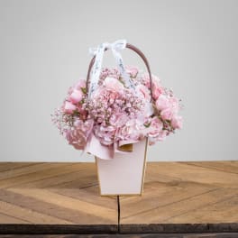 Pink flower arrangement in a white handled box with a ribbon bow