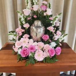 Pink and white floral arrangement surrounding a silver urn on a table