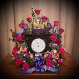 Pink and purple rose arrangement around a clock with crowns and ribbon