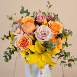 Bouquet of peach and pink roses with yellow lilies in a white vase