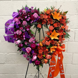 Heart-shaped floral wreath with purple, pink, and orange flowers on a stand