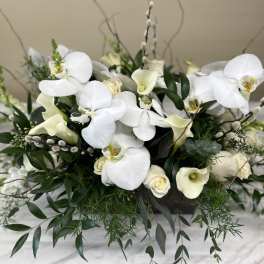 White orchids and calla lilies arranged with greenery in a low container