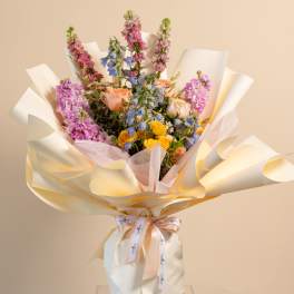 Mixed bouquet of pink, blue, and yellow flowers wrapped in white paper