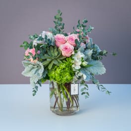 Pink roses and white flowers in a clear glass vase with eucalyptus