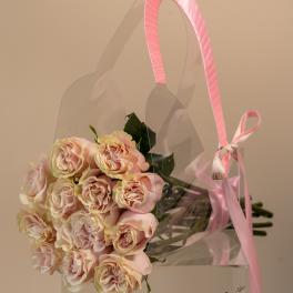 A bouquet of pale pink roses in a clear gift bag with a pink ribbon handle.