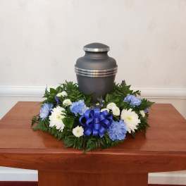 Funeral urn surrounded by blue and white flowers on a table