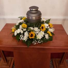 Funeral urn surrounded by white and yellow flowers on a wooden table