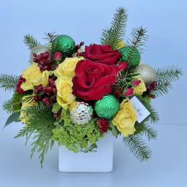 Red and yellow roses arranged in a white box with pine and ornaments