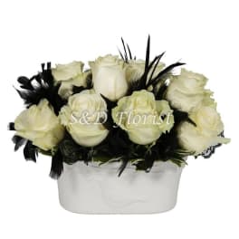 White roses arranged in a white vase with black feathers