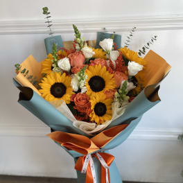 Bouquet of sunflowers, peach roses, and white blooms wrapped in blue and orange paper