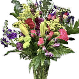 Mixed bouquet of pink, purple, yellow, and red flowers in a clear glass vase