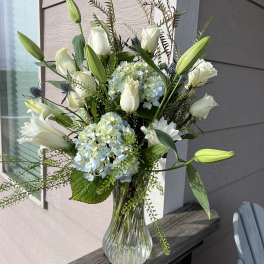 White roses and lilies arranged with blue hydrangeas in a glass vase