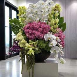 Large arrangement of pink roses and white orchids in a dark bowl