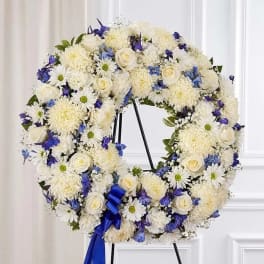 White and blue floral wreath on a black stand with a blue ribbon