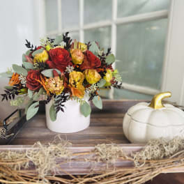 Red and yellow roses in a white vase beside a decorative pumpkin