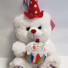 White teddy bear wearing a red birthday hat and holding a birthday cake