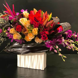 Large bouquet of red, peach, and purple flowers in black wrap