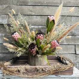 Pink protea arrangement in a wooden container with dried grasses
