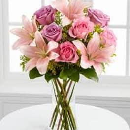 Pink and lavender roses with pale lilies in a clear glass vase
