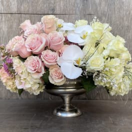 Pink and white roses with orchids in a silver pedestal vase