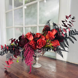 Red roses arranged in a silver pedestal vase with dark foliage