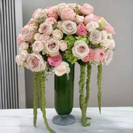 Pink and white rose arrangement in a green glass vase with trailing green accents