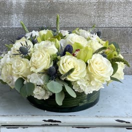 Low floral arrangement of white roses and green blooms in a round container