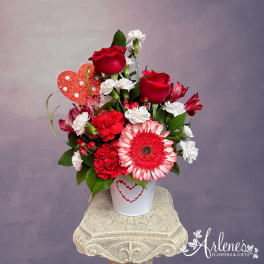 Red and white flower arrangement in a white tin with a heart decoration