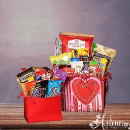 Two red gift boxes filled with assorted chips, candy bars, and popcorn on a wooden tabletop.