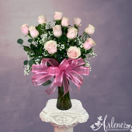 Pink roses arranged in a tall glass vase with a large pink ribbon