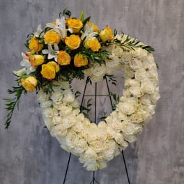 Heart-shaped floral wreath of white and yellow roses on a stand