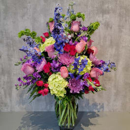 Large mixed bouquet of pink, purple, blue, and green flowers in a glass vase