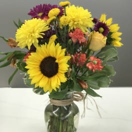 Mixed bouquet with sunflowers, purple daisies, and a yellow rose in a glass vase
