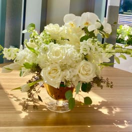 White roses and orchids arranged in a glass compote vase