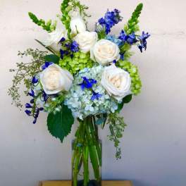 White roses and blue flowers arranged in a tall glass vase