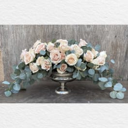 Blush roses arranged in a silver pedestal bowl with trailing eucalyptus