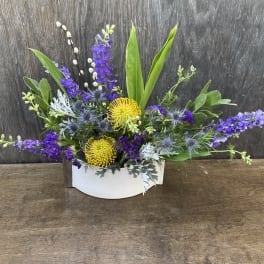 Low floral arrangement with purple and yellow blooms in a white container
