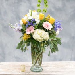 Mixed bouquet in a clear glass vase with yellow, white, pink, and purple flowers