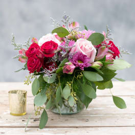 Pink and red roses with purple blooms in a glass vase