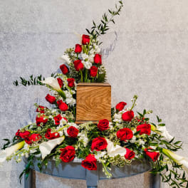 Large floral arrangement with red roses and white calla lilies around a wooden urn
